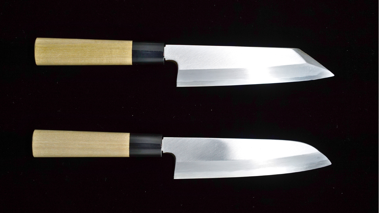Two Japanese kitchen knives, a kiritsuke and a santoku, with wooden handles on a black background.