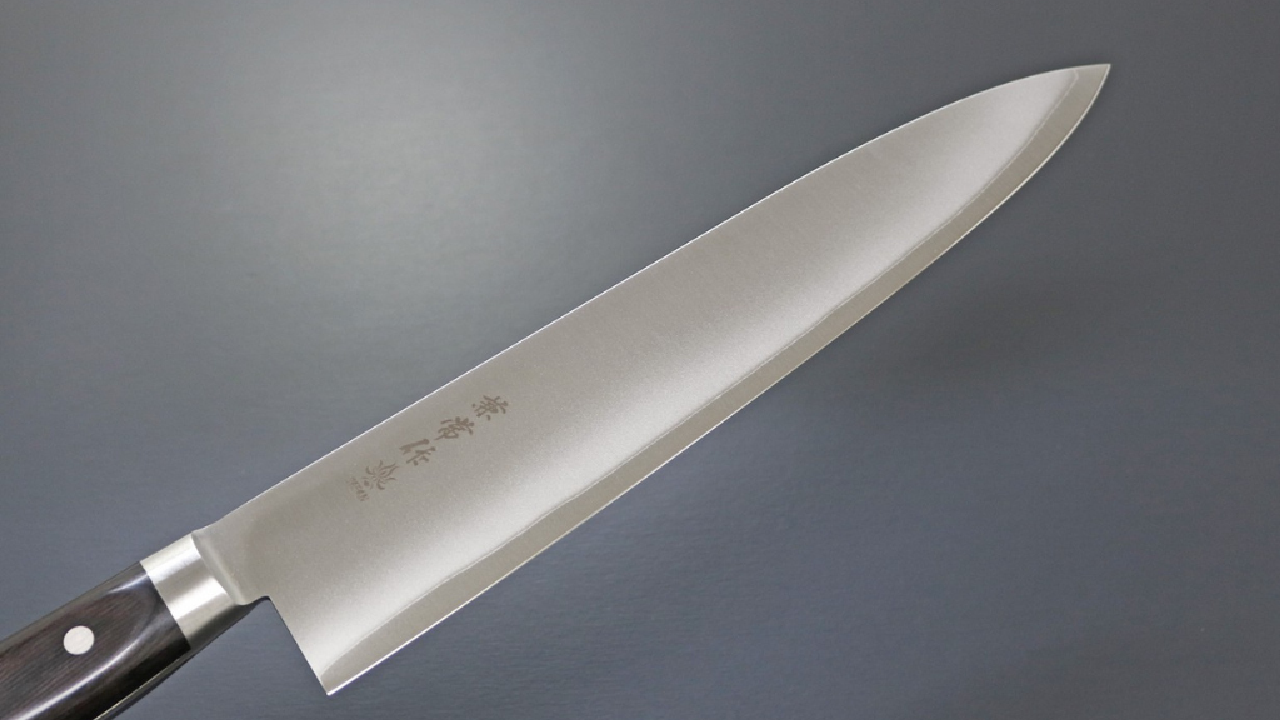 Japanese stainless steel gyuto knife with a dark wooden handle on a gray background.