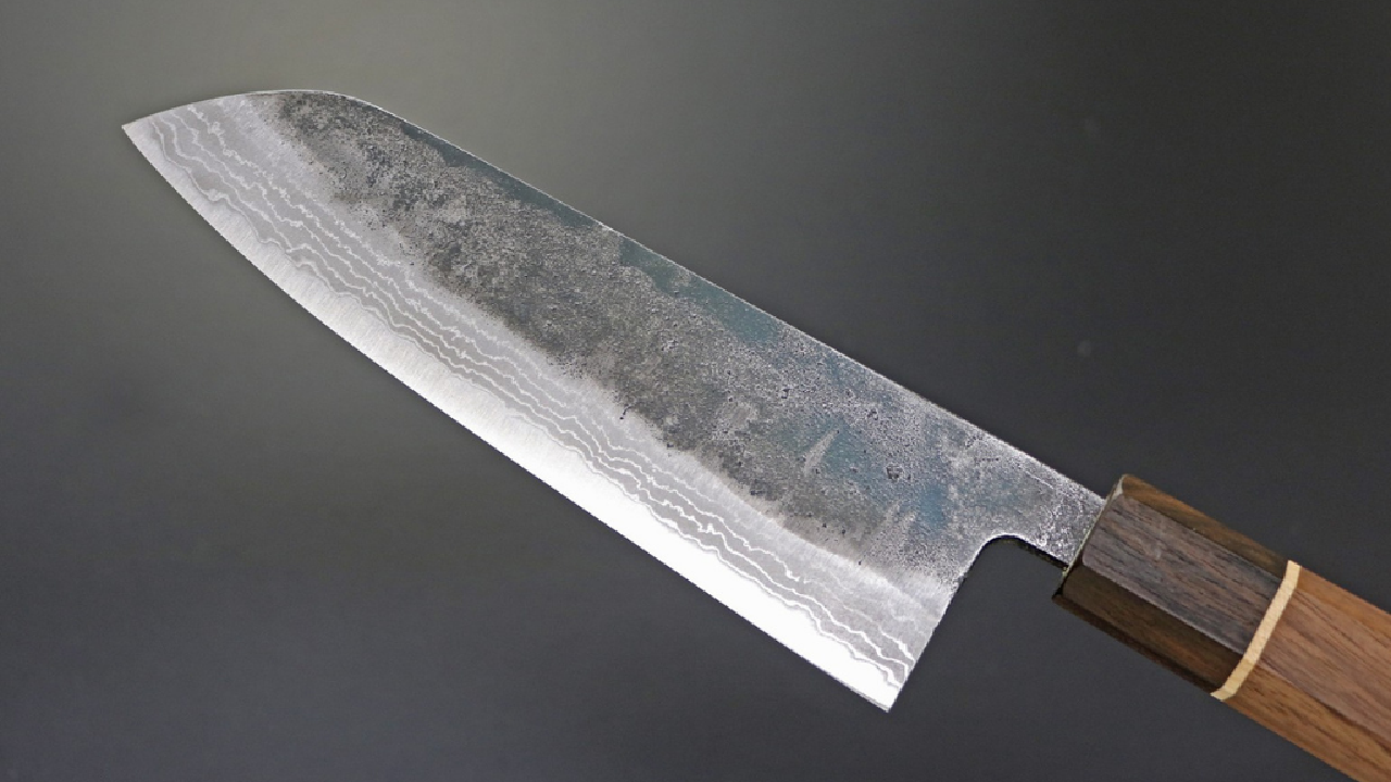 Hand-forged Japanese Damascus kitchen knife with visible layered steel texture and dark wood handle.