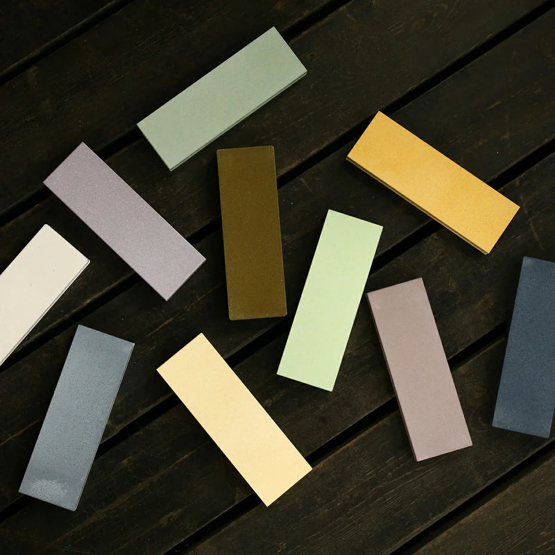 Assorted Shapton ceramic whetstones in various colors arranged on a dark wooden surface.