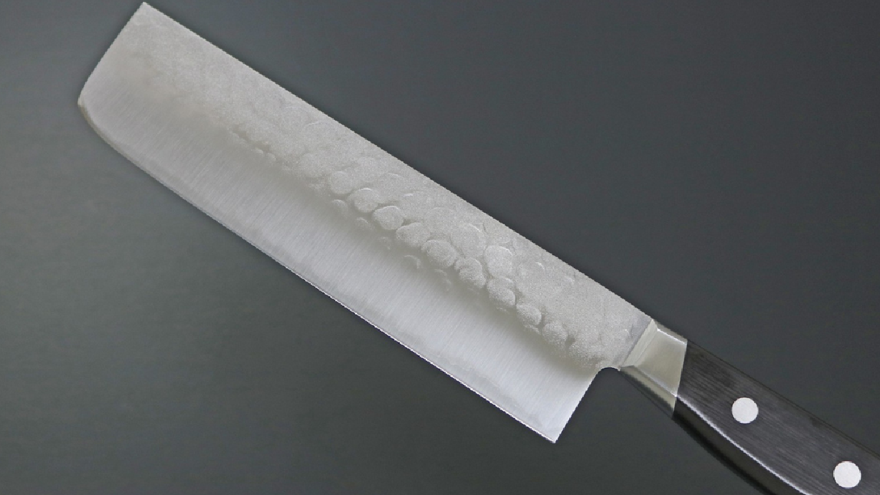 Japanese hammered nakiri knife with double-riveted black handle on a gray background.
