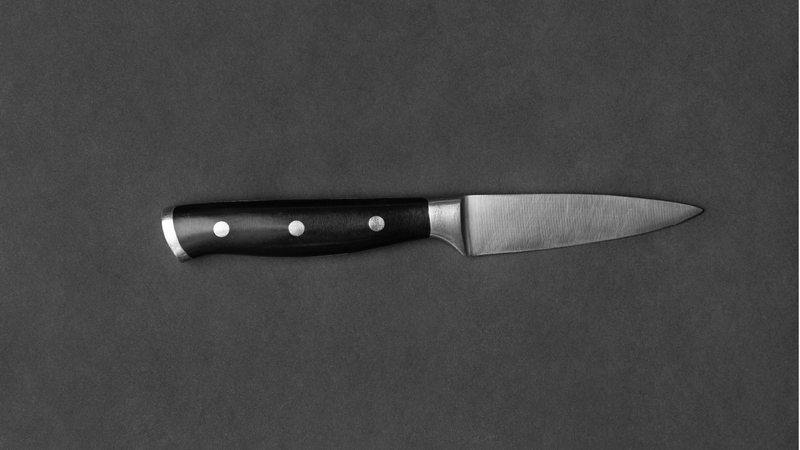 Small paring knife with a black handle placed on a dark gray surface.