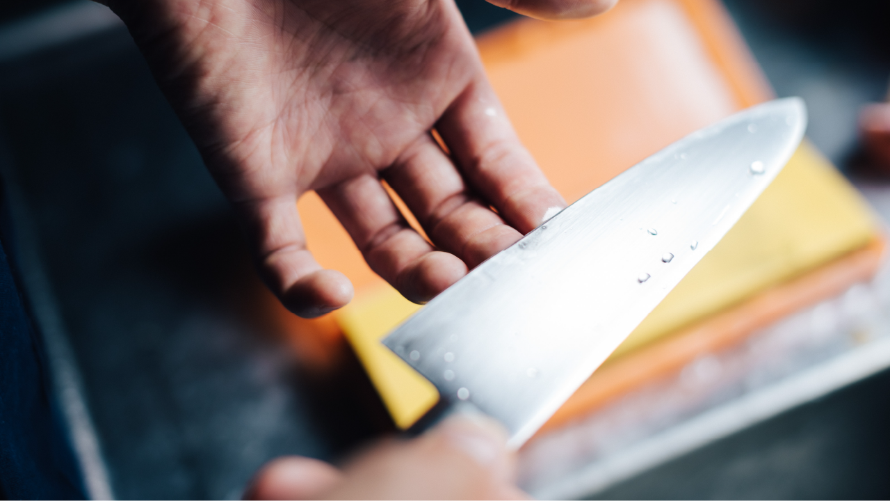 Hand inspecting the sharpness of a freshly sharpened knife with water droplets on the blade.
