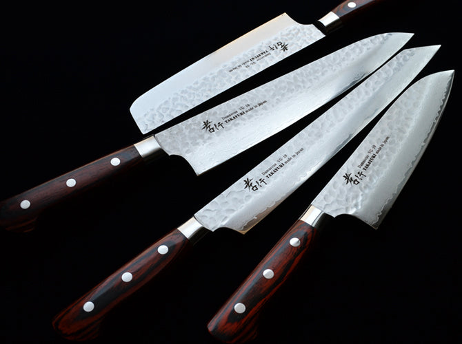 Set of four Japanese chef knives with wooden handles on a black background