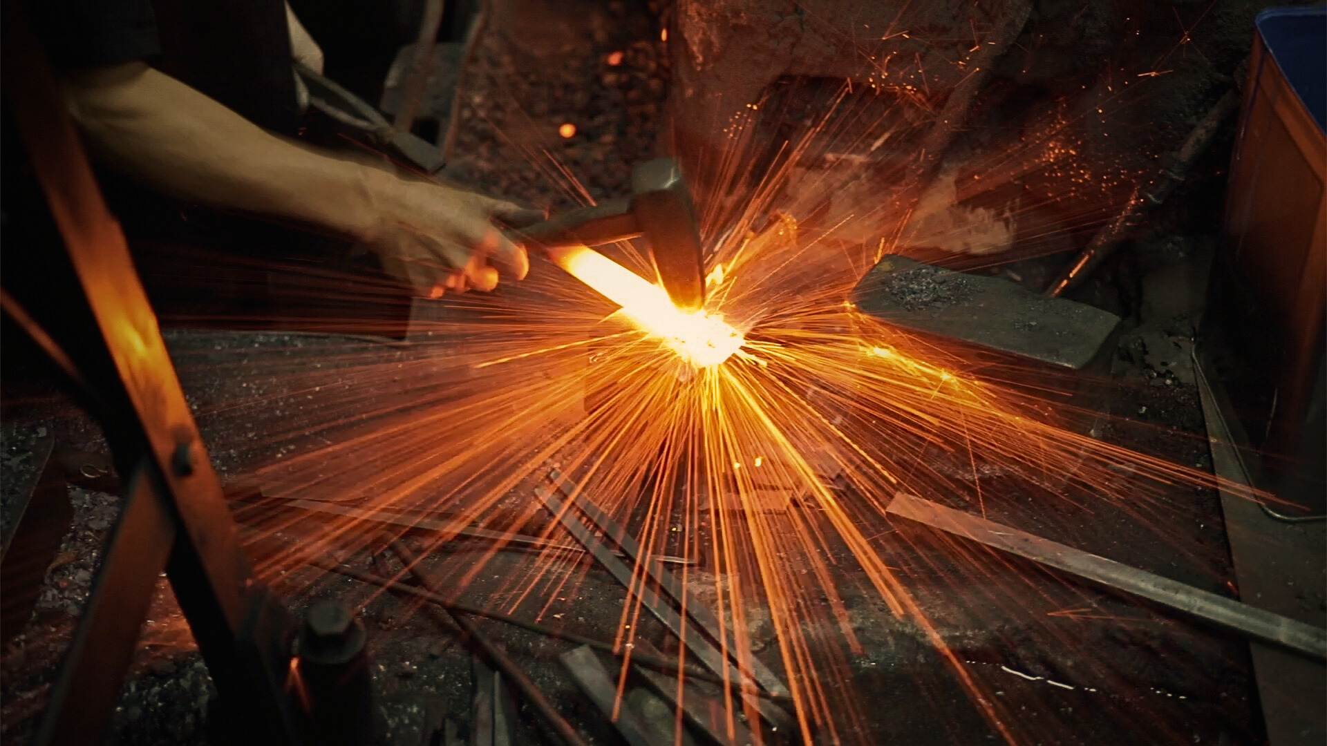 A Japanese blacksmith heating and hammering glowing steel during the knife forging process.