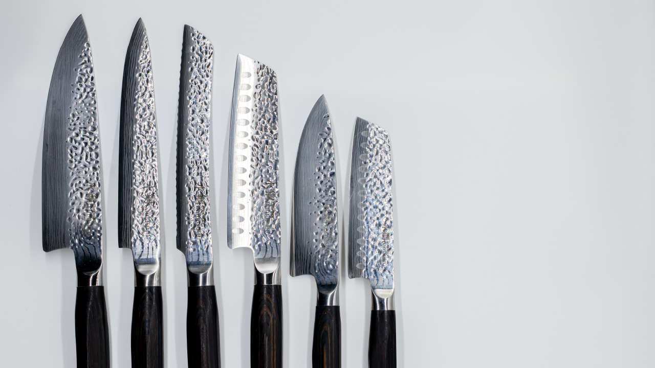 Set of six Japanese Damascus kitchen knives with hammered patterns displayed on a white surface.