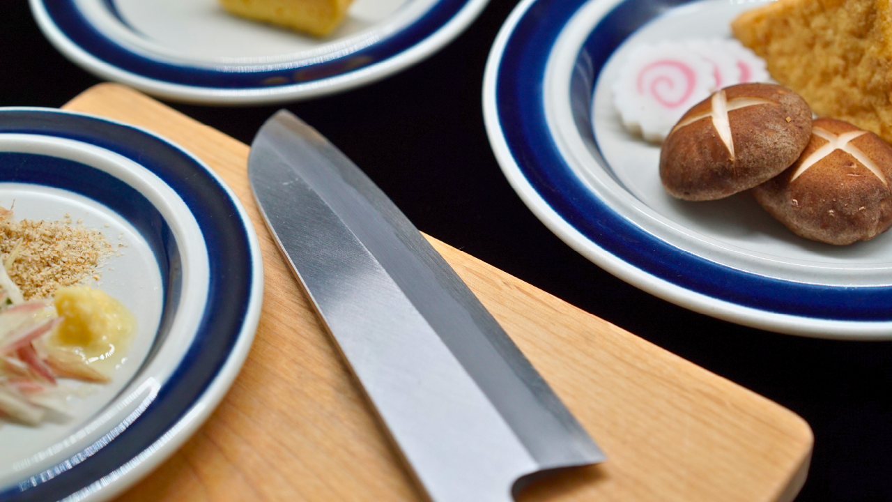 Japanese kitchen knife placed beside traditional Japanese dishes on blue-rimmed plates.