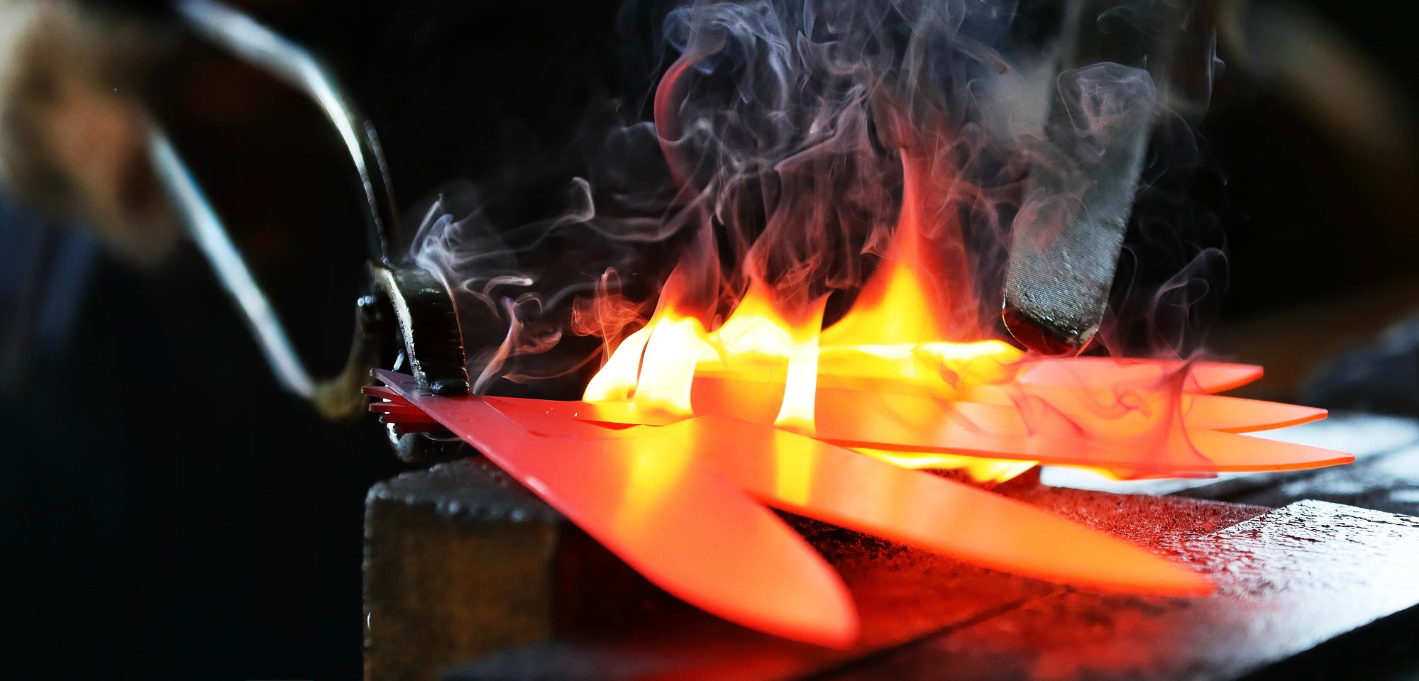 Hot metal object being worked on with flames and smoke in a blacksmithing setting