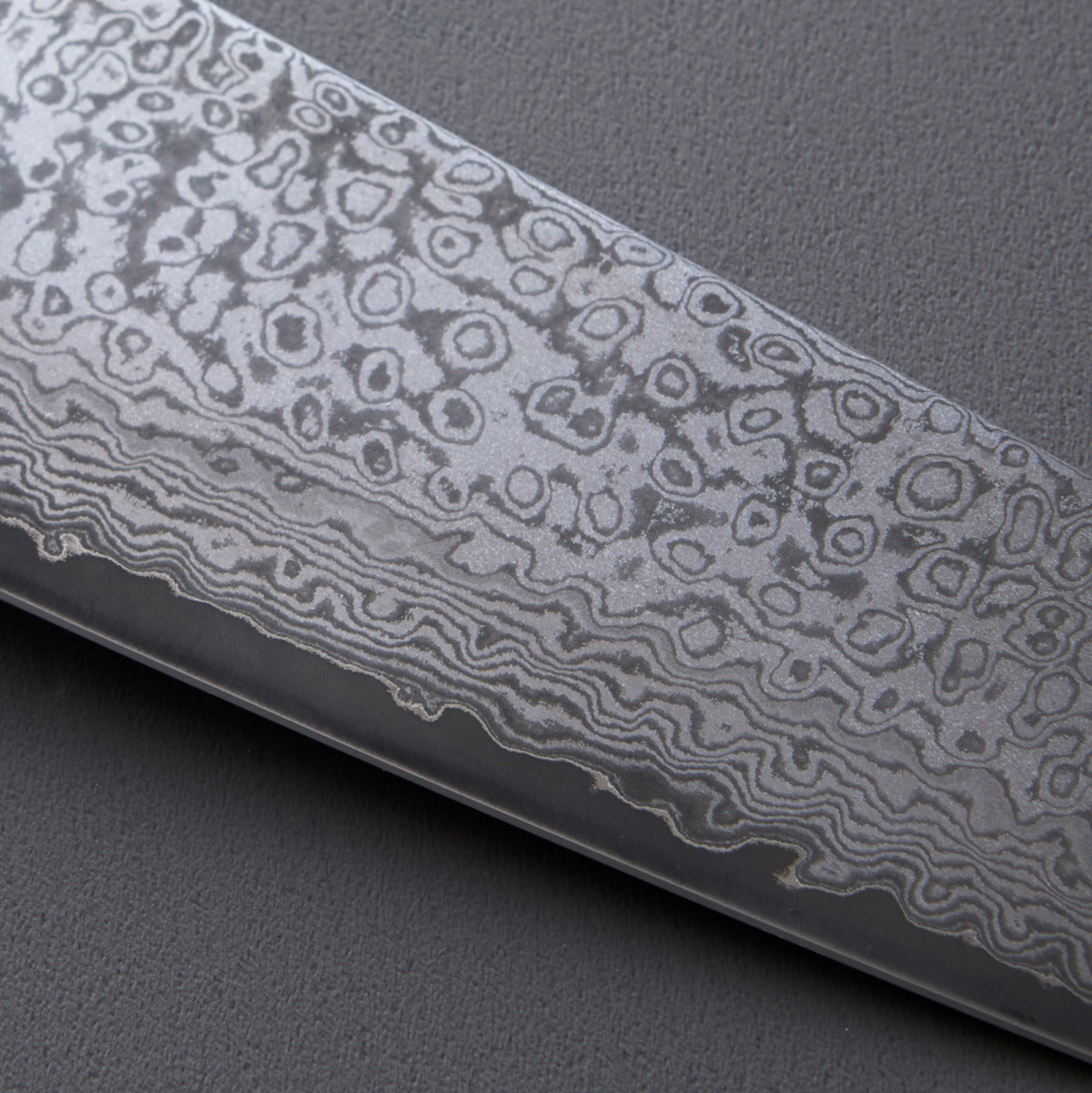 Close-up of a knife blade with a detailed pattern on a gray background