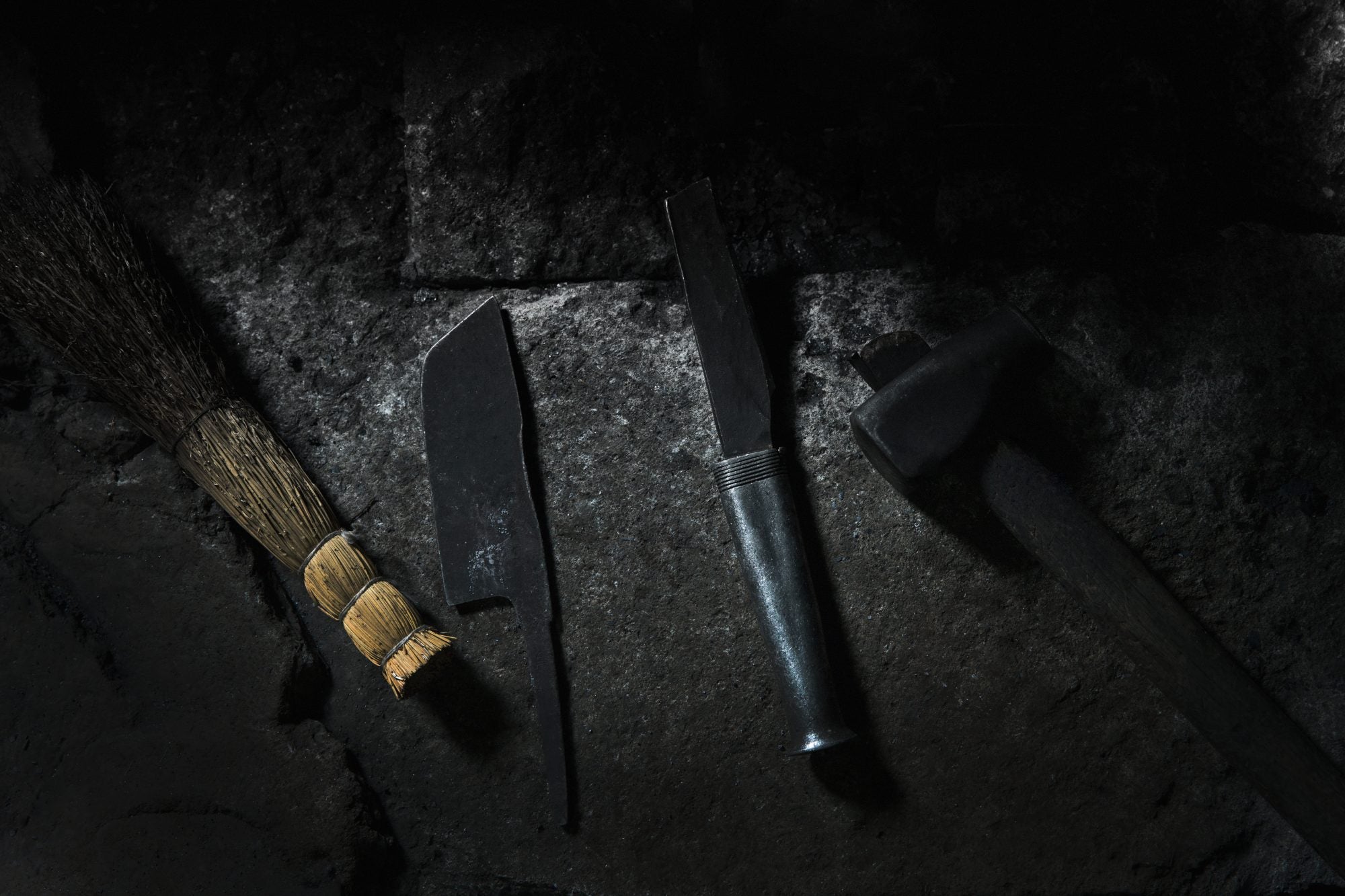 Dark and ominous scene with a broom, cleaver, knife, and hammer on a textured surface.