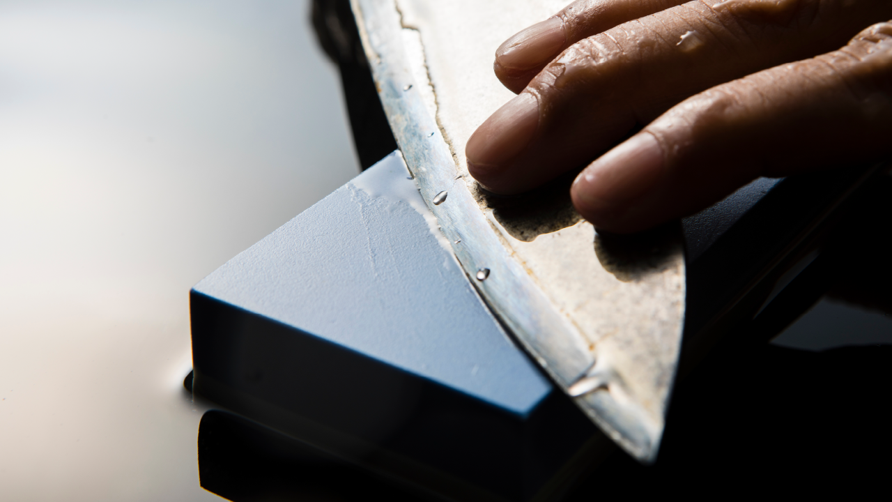 Close-up of a craftsman sharpening a Japanese knife on a whetstone with water droplets on the blade.