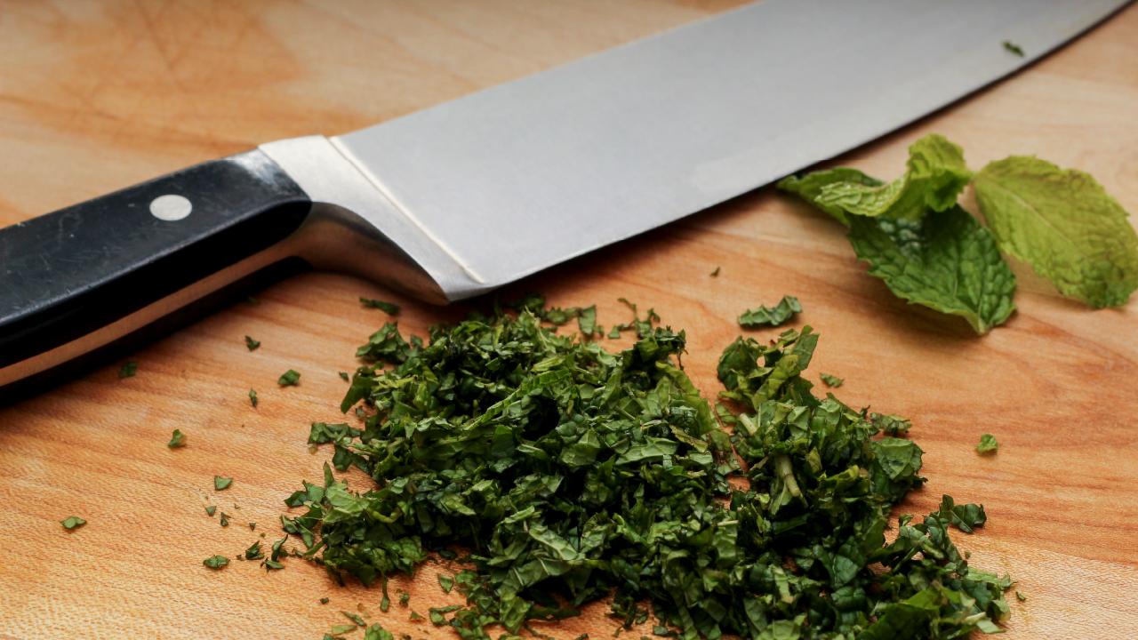 Chopped green herbs on a wooden cutting board with a knife