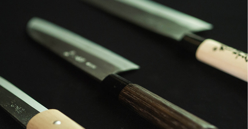 Three traditional Japanese knives on a dark surface