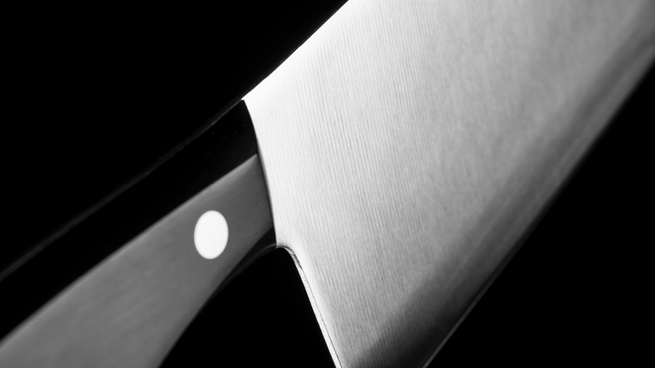 Close-up of a stainless steel Japanese kitchen knife showing the brushed metal texture and polished black handle against a dark background.