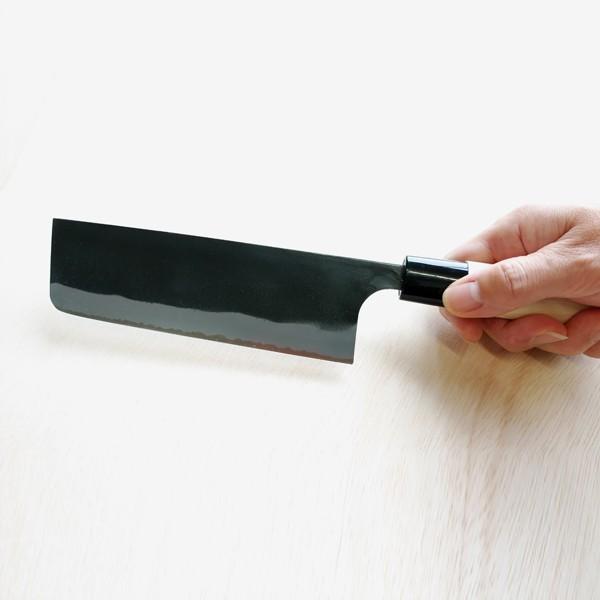 Hand holding a black cleaver over a light-colored wooden surface