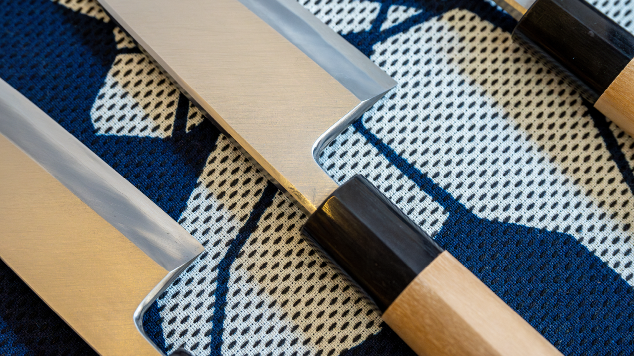 Set of Japanese Santoku knives with wooden handles placed on traditional patterned fabric.