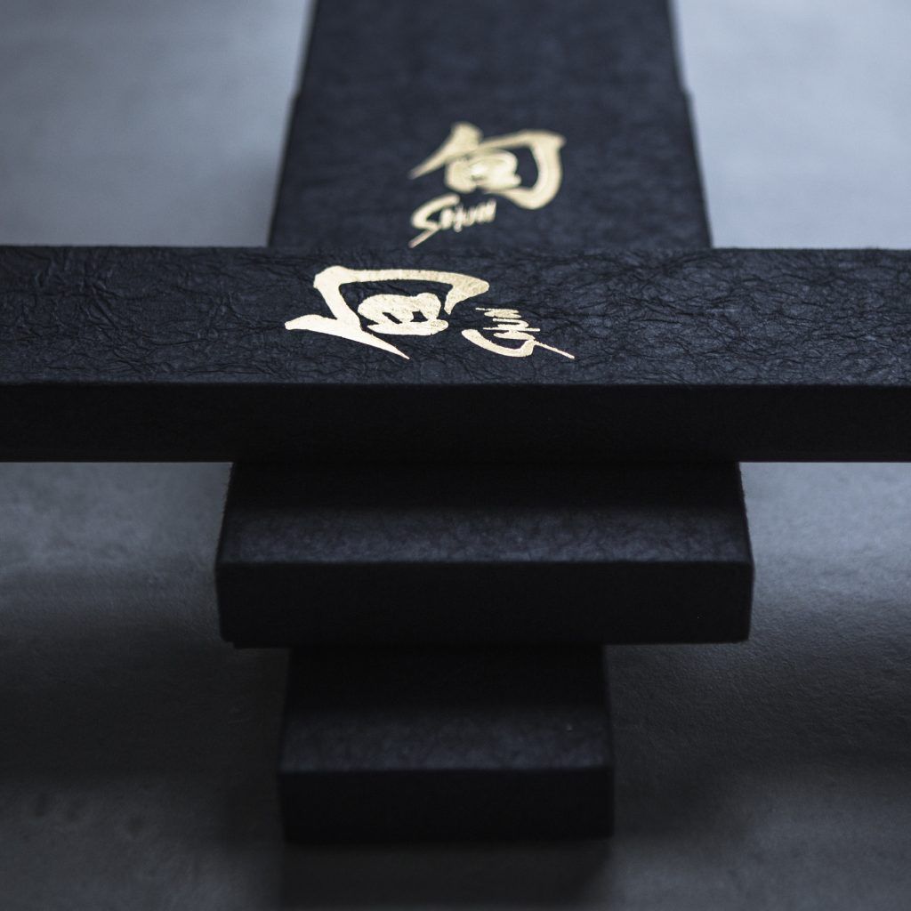Elegant black knife box with gold Japanese calligraphy logo of “Shun” on textured paper surface.